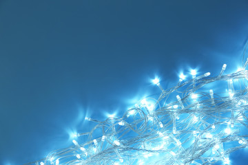 Glowing Christmas lights on turquoise background, top view. Space for text