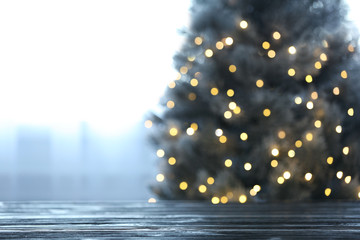 Blurred view of beautiful Christmas tree with yellow lights near window indoors, focus on wooden...
