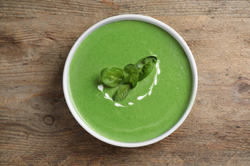 Bowl of healthy green soup with fresh spinach on wooden table, top view