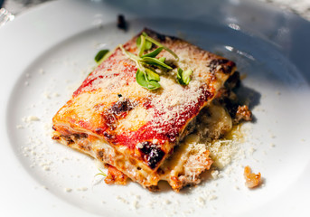 Lasagna with beef, tomatoes and eggplant, powdered with mozzarella. Restaurant serving. Lasagna on white plate.