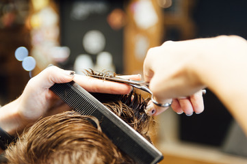 The hands of young barber making haircut to attractive man in barbershop