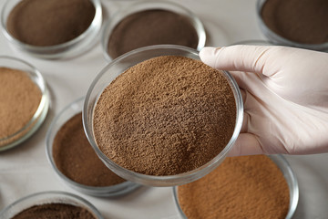 Woman holding Petri dish with soil sample over table, closeup. Laboratory research