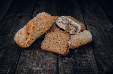 Fresh crisp bread on a dark wooden background. The concept of baking bread, eating meals with rolls, bread. Product made of wheat and rye flour, bread preparation. Eating sandwiches.