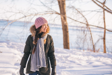 Winter woman walking out on forest walk in cold outdoor nature river outside. Happy asian girl model wearing wool hat, scarf and fur jacket outerwear enjoying outdoors winter background.