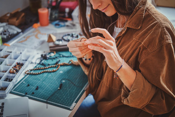 Happy smiling woman is working on beads jewellery at her own workplace.