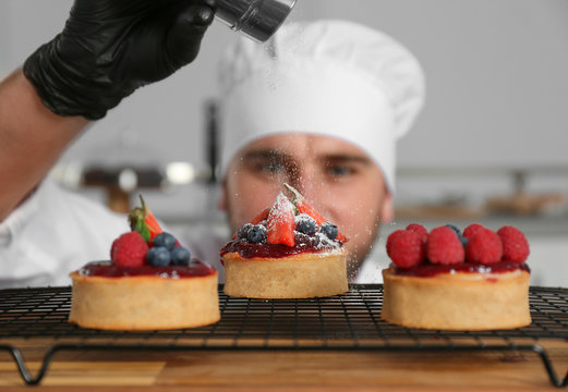 Male pastry chef sprinkling desserts with sugar powder in kitchen