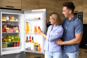 Couple taking bottle with juice out of refrigerator in kitchen