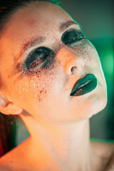 A stunning make-up on the face of a beautiful young girl, beauty makeup, oil on her face and sparkly green with priority red