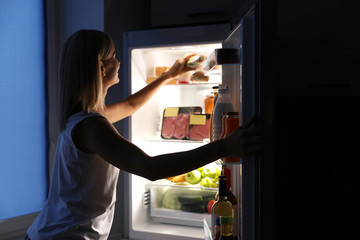 Fototapeta na wymiar Woman taking sandwich out of refrigerator in kitchen at night