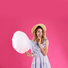 Happy young woman with cotton candy on pink background