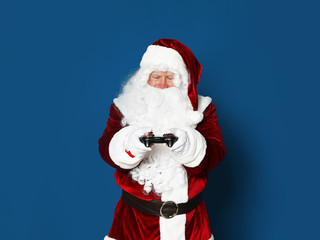 Fototapeta na wymiar Authentic Santa Claus with game controller on blue background. Space for text