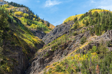 Low angle landscape of tall granite mountain with yellow and green aspen trees near Ouray, Colorado