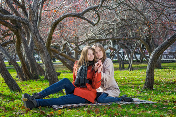 Two pretty girlfriends are sitting on lawn in park