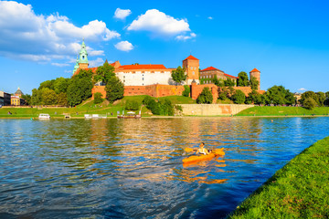 Unidentified young woman paddling in yellow kayak on Vistula river with Wawel castle in background,...