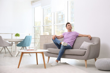 Young man relaxing on sofa under air conditioner at home