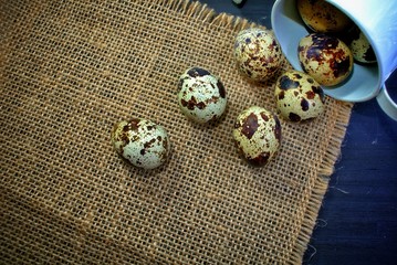 Quail eggs on sackcloth and a black wooden background.