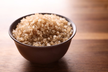 Bowl with brown sea salt on wooden table, closeup. Spa treatment