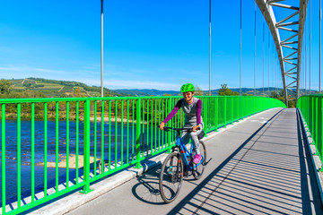Young woman on bicycle riding on bridge crossing Dunajec river near Nowy Sacz, Poland