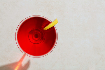 Fototapeta na wymiar Red cocktail in martini glass with lemon under hard summer sunlight
