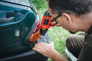 Young man repair a bumper on his car using a drill
