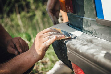 A mechanic repairing a bumper on the car and prepairing surface with sandpaper