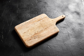A Cutting board with handle on black stone table. Empty pine wooden chopping board on dark...