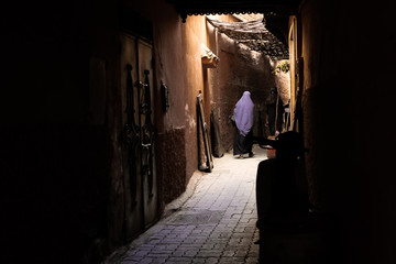 Naklejka na ściany i meble Moroccan Woman Walking Down A Narrow Alley In Jamaa El Fnaa Market Square, Marrakesh, Morocco