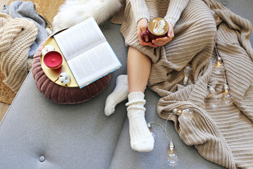 Top view of woman relaxing on couch at home, drinking latte. Cozy evening at home. Young woman enjoying alone time, sitting on sofa covered with soft blanket. Close up, copy space.