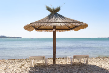 Vacation background. Big umbrella in a center and two loungers on a beach. View from behind. Sunny day.