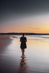 A calm and peaceful with a girl standing on the beach an waves with perfect sunset reflection on a holiday evening. Praia da Bordeira at the Algarve Coast in Portugal, Atlantic Ocean