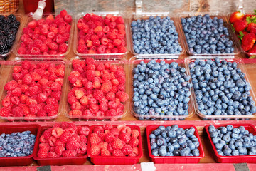 Fresh blueberries and raspberries displayed in plastic containers on an outdoor market stall
