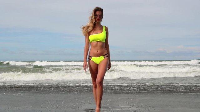 Beautiful young woman in neon yellow bikini swimsuit. Concept of fitness healthy active living. Sport and travel. Weight loss and body image concept. Girl with perfect fit body on tropical beach.
