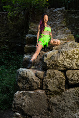 Naklejka premium Asian tattooed woman in neon rave clothing poses on an abandoned rock wall in the forest
