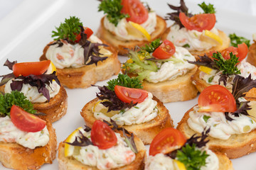 Closeup of delicious canape served on white plate during wedding celebration. Yummy bread with cheese, tomatoes and greens. Concept od catering, appetizer and snack.