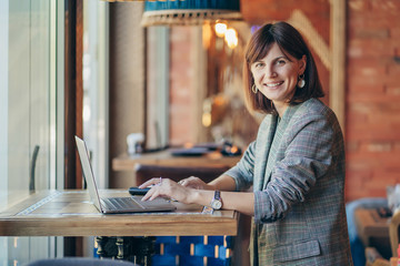 Portrait of a young business woman in gray blazer   at cafe and working on net-book.  Freelancer working in coffee shop.