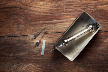 Vintage glass syringe in a metal box and needles on wooden table