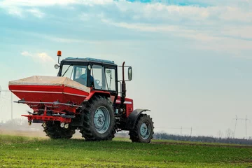 Tuinposter Agricultural tractor fertilizing wheat crop field with NPK © Bits and Splits