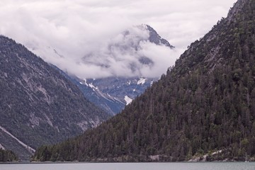 Hoher Berg in Wolken an regnerischem Tag mit einem See im Vordergrund