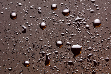 Shiny water drops on a dark brown moody surface
