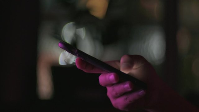 Close up woman hands using smart phone in dark room in front of computer monitor.