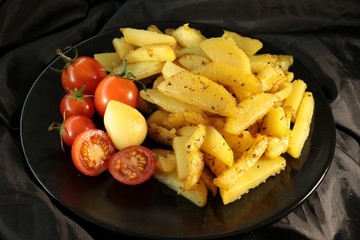 fried potatoes with spices, garlic and red cherry tomatoes on a black plate