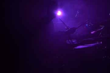 The silhouette of a drummer playing a drum kit on stage in the rays of light from spotlights. Rock concert.