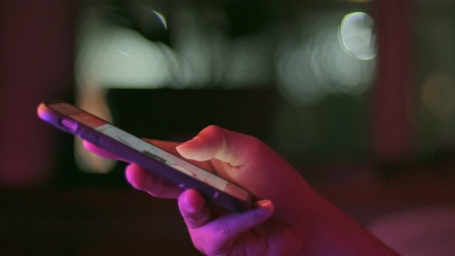 Gadget technology or communication concept : Close up woman hands using smart phone in dark room in front of computer monitor.