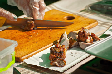 The cook slices the meat with a knife. Glove hand holding knife closeup. Slice of fried meat on a wooden board.
