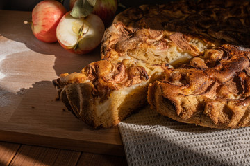 homemade apple pie and fresh apples on a wooden table in the kitchen, piece of pie