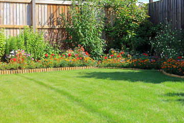 Summer Flower Borders Surrounding A Grass Lawn In An Enclosed Home Garden.