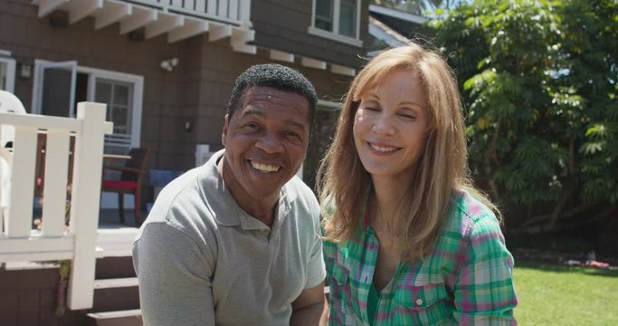 Portrait of husband and wife gardening in their backyard smiling at camera. Close up of Happy African American and Caucasian couple outside at home. Slow motion 4k Handheld