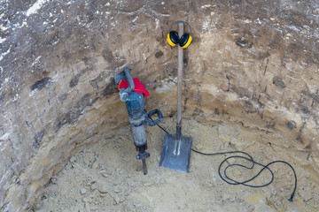Digging drilling pit service company. Jackhammer, shovel, safety gloves and ear muffs in deep pit. Dig work.