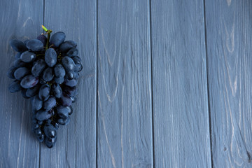 Photo of a bunch of grapes on a gray wooden background. Blue grapes with copy space