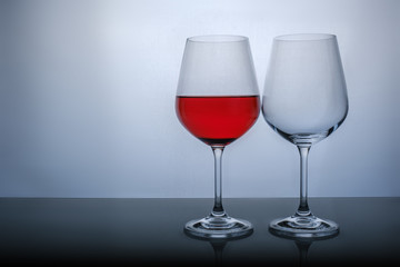 one glass half full of red wine, and the second empty on a white background.